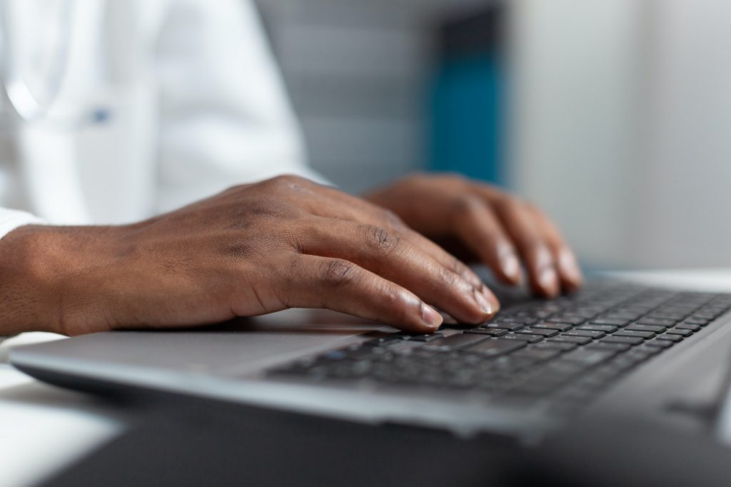 Closeup of african american doctor hand typing healthcare treatment on laptop computer